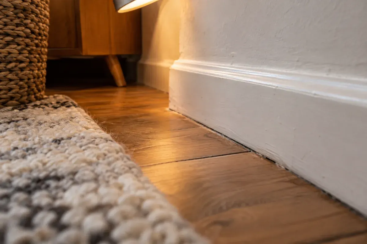 Angle entre une plinthe, un parquet et le bord d’un tapis.
